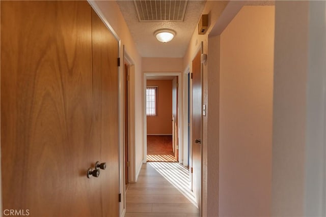 corridor featuring light wood-style floors, baseboards, visible vents, and a textured ceiling