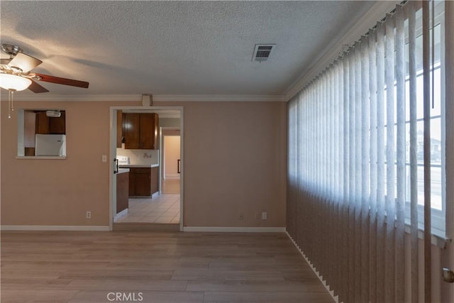 unfurnished room with visible vents, light wood-style flooring, ornamental molding, a textured ceiling, and baseboards