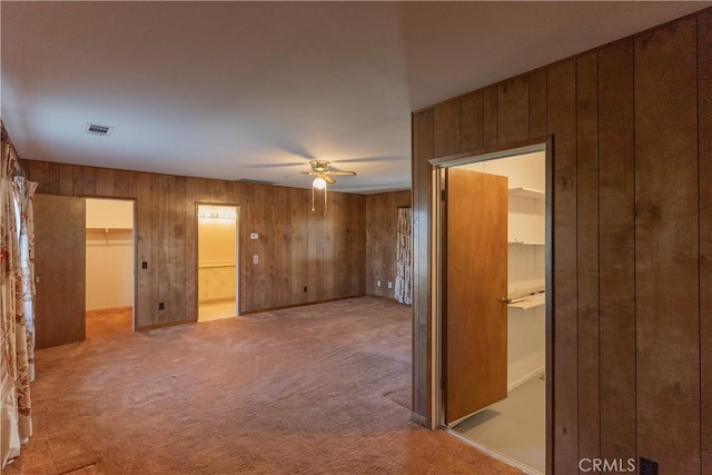 unfurnished room featuring light carpet, wood walls, ceiling fan, and visible vents