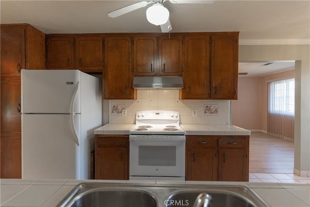 kitchen with brown cabinets, tile counters, decorative backsplash, white appliances, and under cabinet range hood