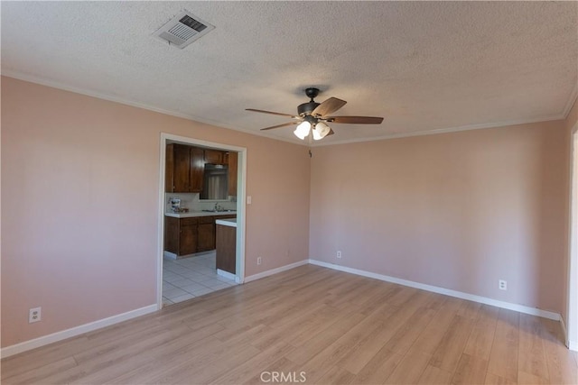 spare room featuring visible vents, light wood-style floors, ornamental molding, ceiling fan, and baseboards