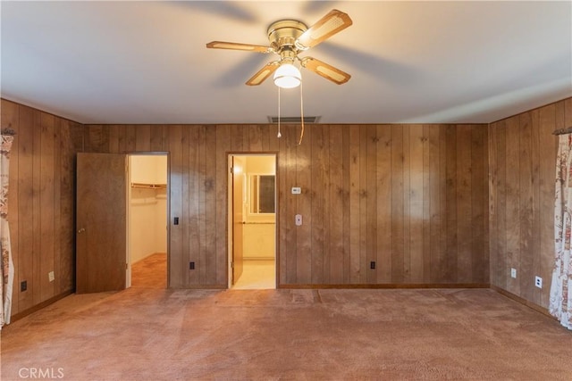 unfurnished bedroom featuring light carpet, visible vents, a spacious closet, and wooden walls