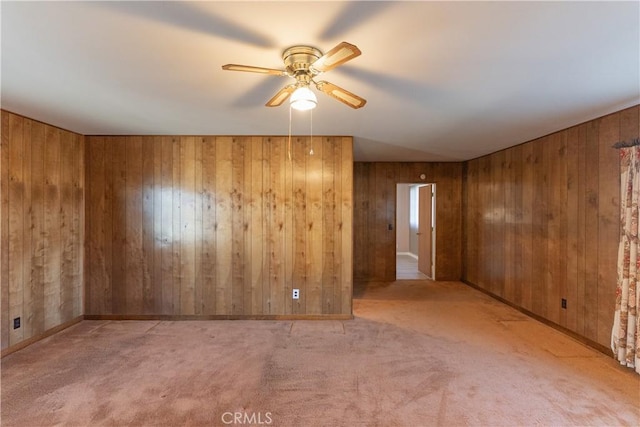 empty room featuring a ceiling fan, light carpet, and wood walls