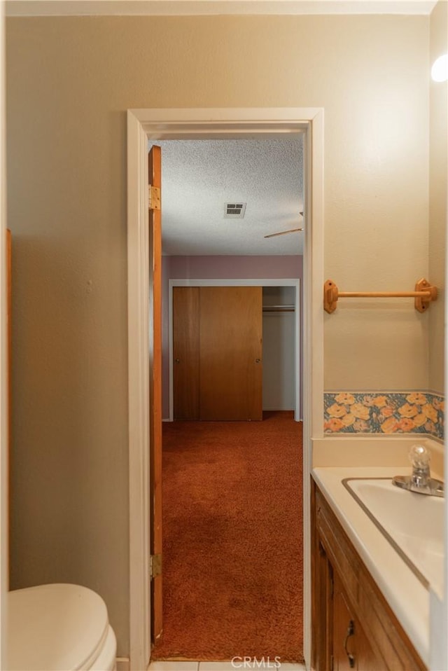 half bath with visible vents, toilet, vanity, and a textured ceiling