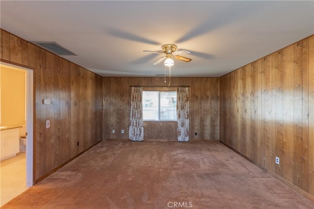 spare room featuring wood walls, light colored carpet, visible vents, and a ceiling fan