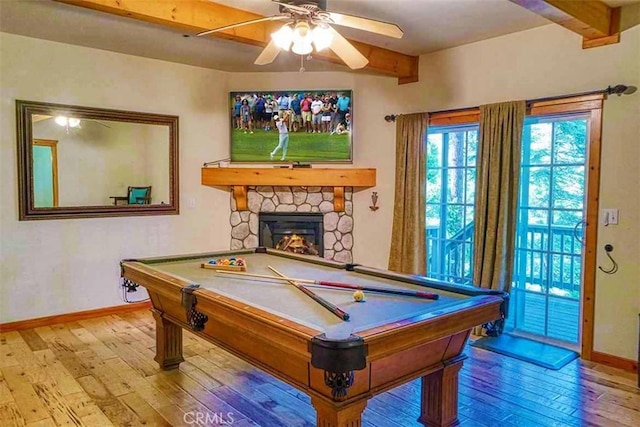 game room featuring billiards, a stone fireplace, ceiling fan, beam ceiling, and light hardwood / wood-style floors