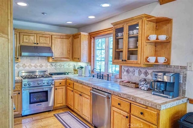 kitchen with sink, light hardwood / wood-style flooring, appliances with stainless steel finishes, tile counters, and backsplash