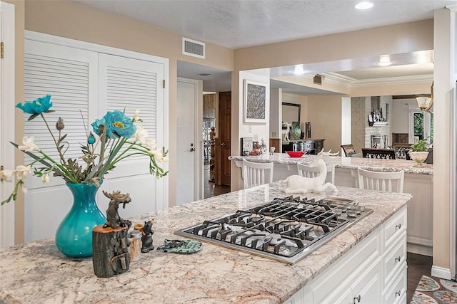 kitchen with a fireplace, ornamental molding, light stone countertops, stainless steel gas cooktop, and white cabinets