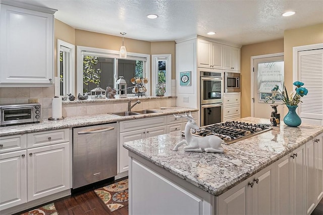 kitchen with pendant lighting, sink, white cabinets, and appliances with stainless steel finishes