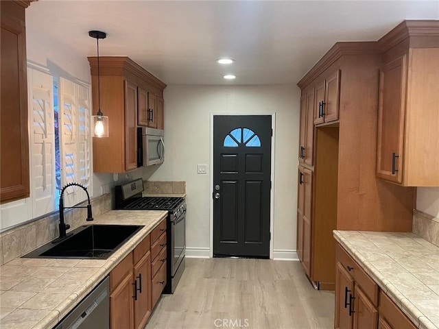 kitchen featuring stainless steel appliances, sink, tile counters, and light hardwood / wood-style flooring