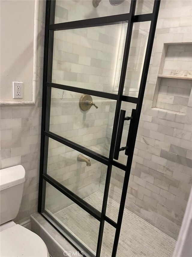 bathroom featuring toilet, tile walls, and a tile shower