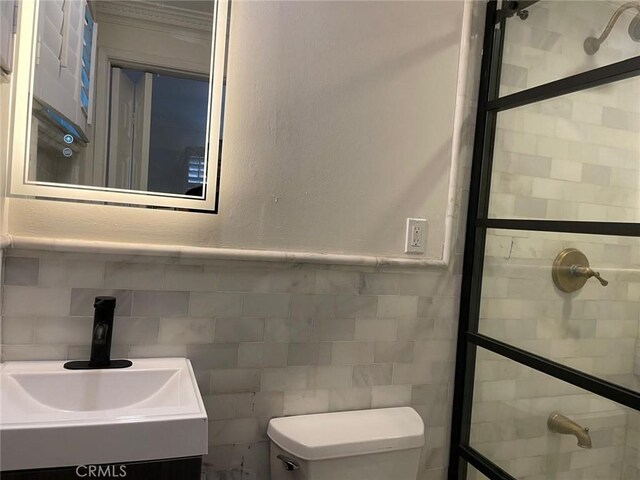 bathroom with vanity, tiled shower, tile walls, and toilet