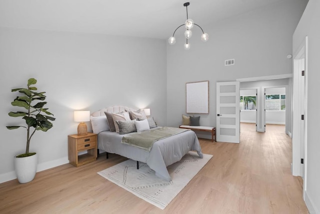 bedroom featuring high vaulted ceiling, light hardwood / wood-style flooring, and a notable chandelier