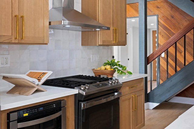 kitchen with tasteful backsplash, appliances with stainless steel finishes, wood-type flooring, and wall chimney range hood