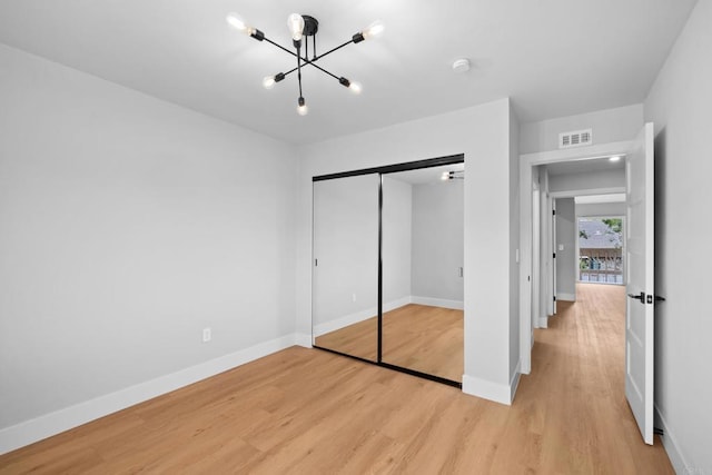 unfurnished bedroom featuring a notable chandelier, light wood-type flooring, and a closet