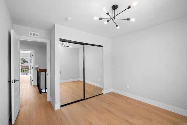 unfurnished bedroom featuring hardwood / wood-style flooring, a notable chandelier, and a closet