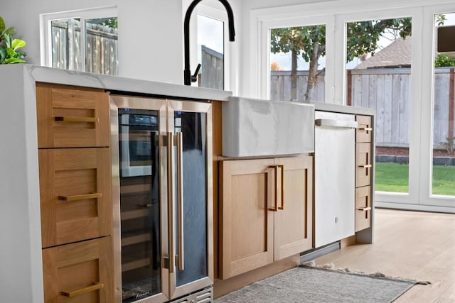 kitchen with light wood-type flooring, a wealth of natural light, beverage cooler, and light brown cabinets