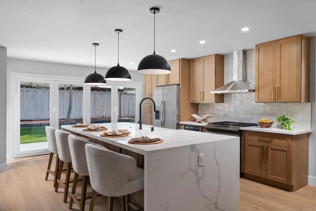 kitchen with pendant lighting, appliances with stainless steel finishes, backsplash, an island with sink, and wall chimney exhaust hood