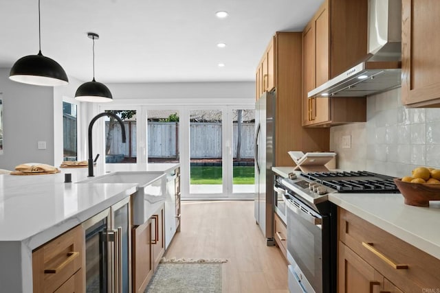 kitchen featuring sink, appliances with stainless steel finishes, decorative backsplash, decorative light fixtures, and wall chimney exhaust hood