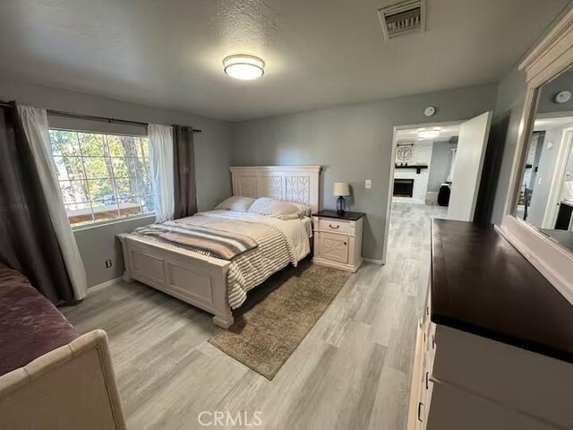 bedroom with a large fireplace and light hardwood / wood-style flooring