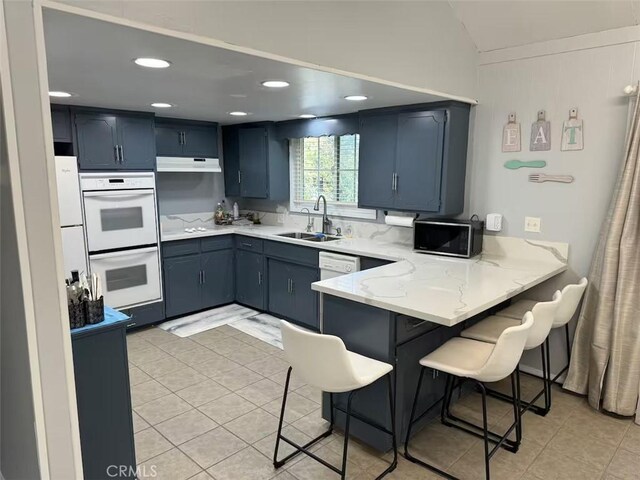 kitchen with light tile patterned flooring, sink, a breakfast bar area, white double oven, and kitchen peninsula