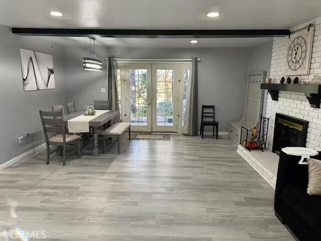 dining area featuring a brick fireplace, wood-type flooring, french doors, and beamed ceiling