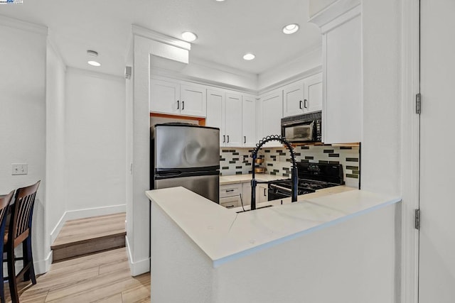 kitchen with tasteful backsplash, black appliances, kitchen peninsula, light hardwood / wood-style floors, and white cabinets