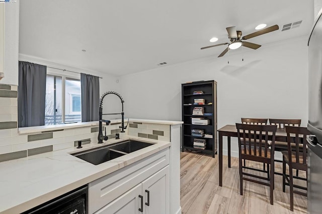 kitchen with sink, light stone counters, tasteful backsplash, dishwashing machine, and white cabinets