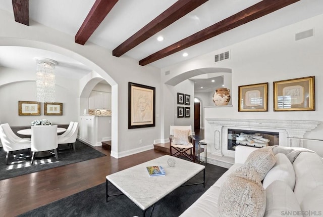 living room featuring beamed ceiling, a premium fireplace, dark wood-type flooring, and a chandelier