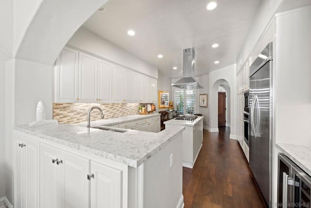 kitchen with white cabinetry, island range hood, kitchen peninsula, and light stone countertops