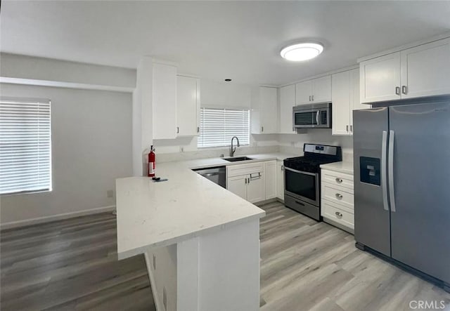 kitchen with sink, white cabinetry, appliances with stainless steel finishes, kitchen peninsula, and light hardwood / wood-style floors