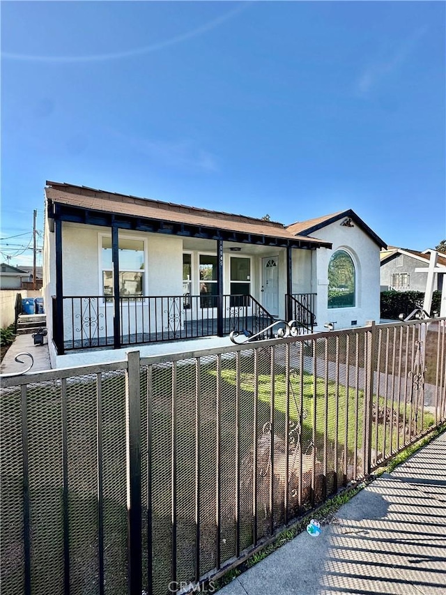 ranch-style home featuring covered porch, a fenced front yard, and stucco siding