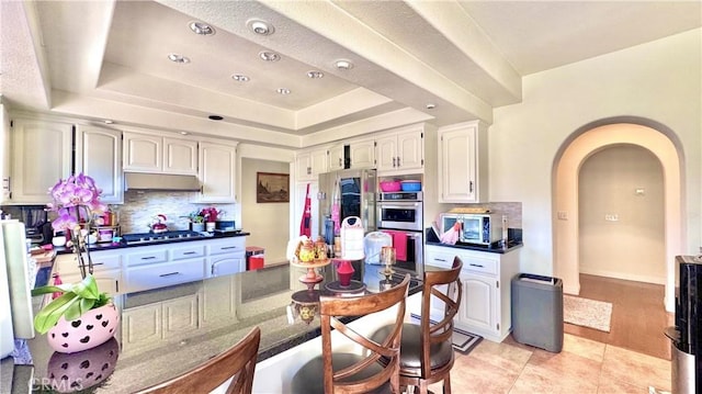 kitchen with stainless steel appliances, a tray ceiling, white cabinets, light tile patterned flooring, and decorative backsplash