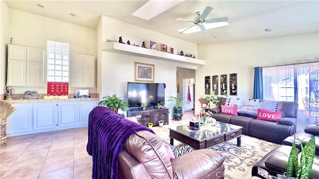 tiled living room with ceiling fan and lofted ceiling with skylight