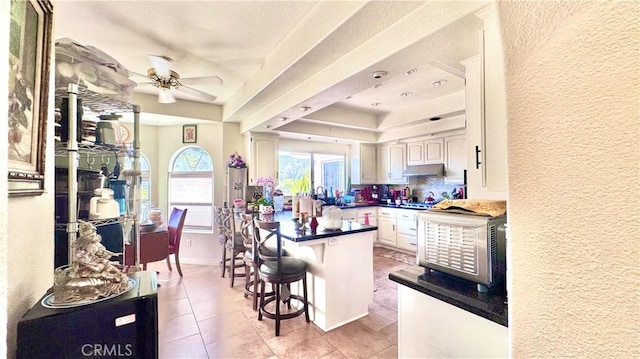 kitchen with kitchen peninsula, a breakfast bar, ceiling fan, and light tile patterned flooring