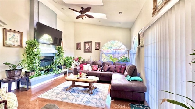 living room featuring hardwood / wood-style flooring, high vaulted ceiling, ceiling fan, and a skylight