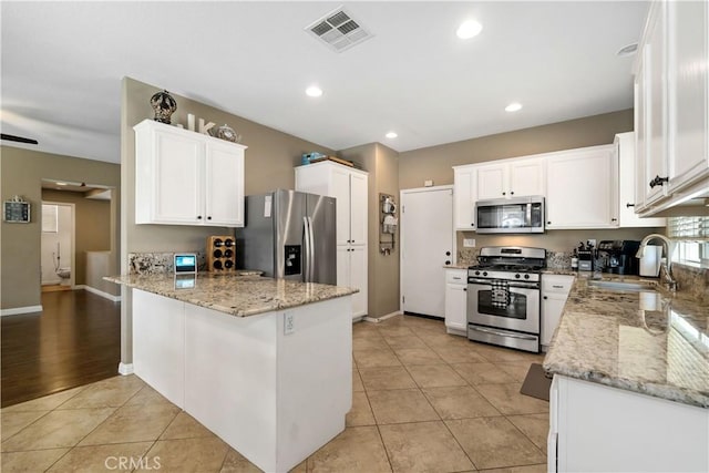 kitchen with sink, appliances with stainless steel finishes, kitchen peninsula, light stone countertops, and white cabinets