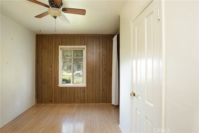 spare room featuring wooden walls, light hardwood / wood-style floors, and ceiling fan