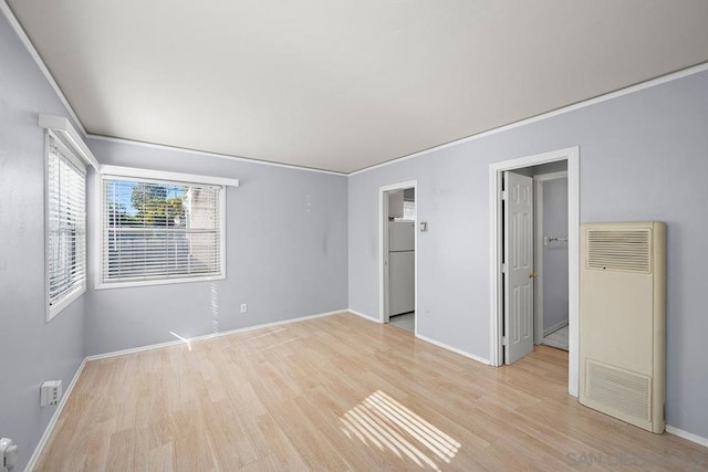 unfurnished bedroom with white refrigerator, ornamental molding, a walk in closet, and light wood-type flooring