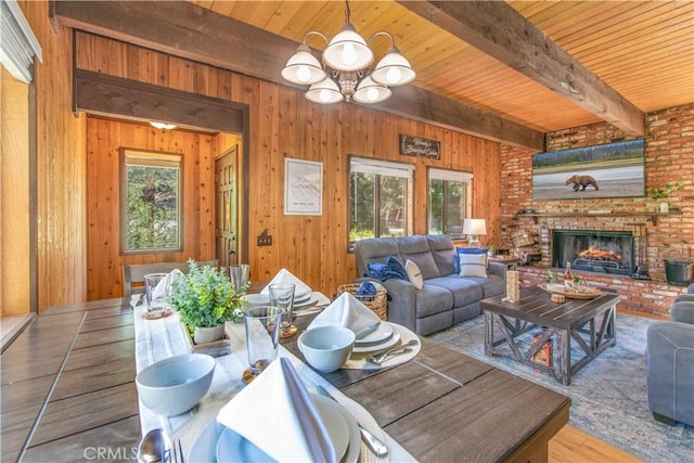 living room featuring hardwood / wood-style floors, wooden walls, a fireplace, beam ceiling, and an inviting chandelier