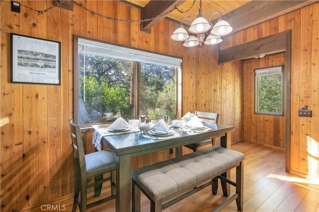 dining area with beam ceiling, a notable chandelier, light hardwood / wood-style floors, and wood walls