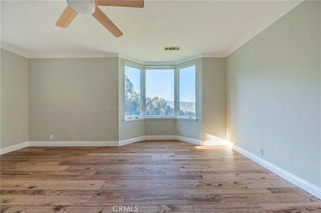 spare room with visible vents, baseboards, crown molding, and wood finished floors