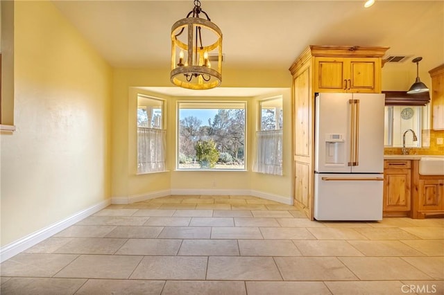 kitchen featuring light tile patterned floors, white refrigerator with ice dispenser, a chandelier, light countertops, and decorative light fixtures