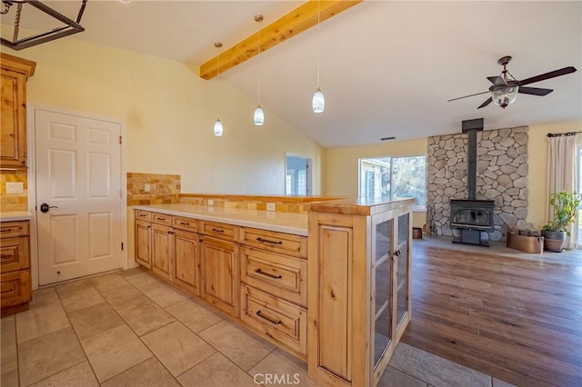 kitchen with light countertops, a wood stove, ceiling fan, a peninsula, and vaulted ceiling with beams