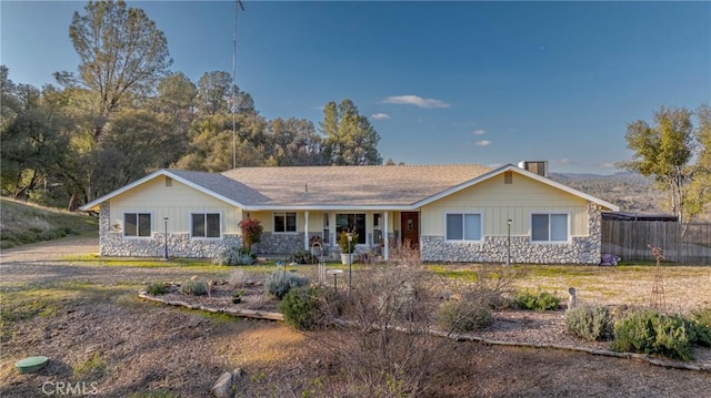 ranch-style home featuring stone siding, fence, a chimney, and covered porch