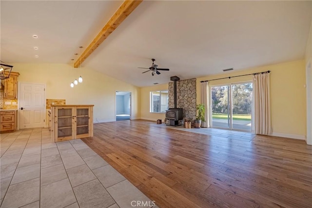 unfurnished living room with a wood stove, lofted ceiling with beams, light wood-type flooring, a ceiling fan, and visible vents