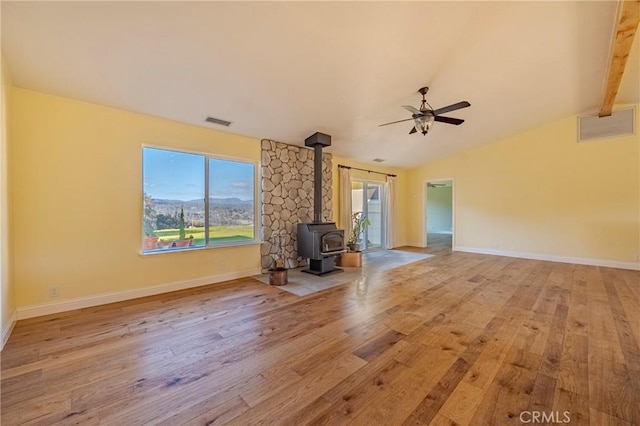 unfurnished living room with lofted ceiling with beams, light wood-style flooring, a wood stove, and baseboards