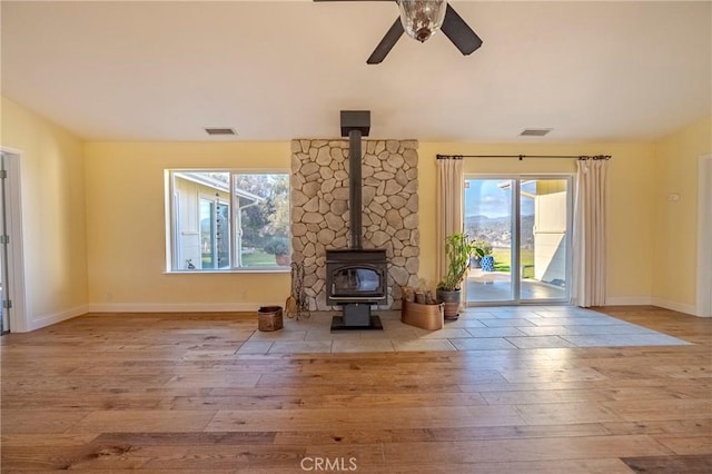 unfurnished living room with a wood stove, light wood-type flooring, and visible vents