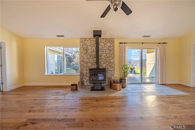 unfurnished living room with a wealth of natural light, a wood stove, wood-type flooring, and visible vents