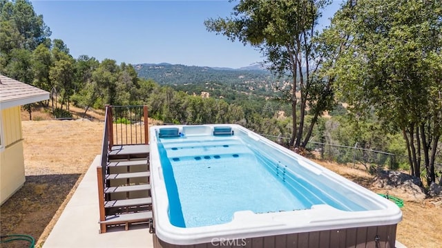 view of pool with a forest view and a hot tub